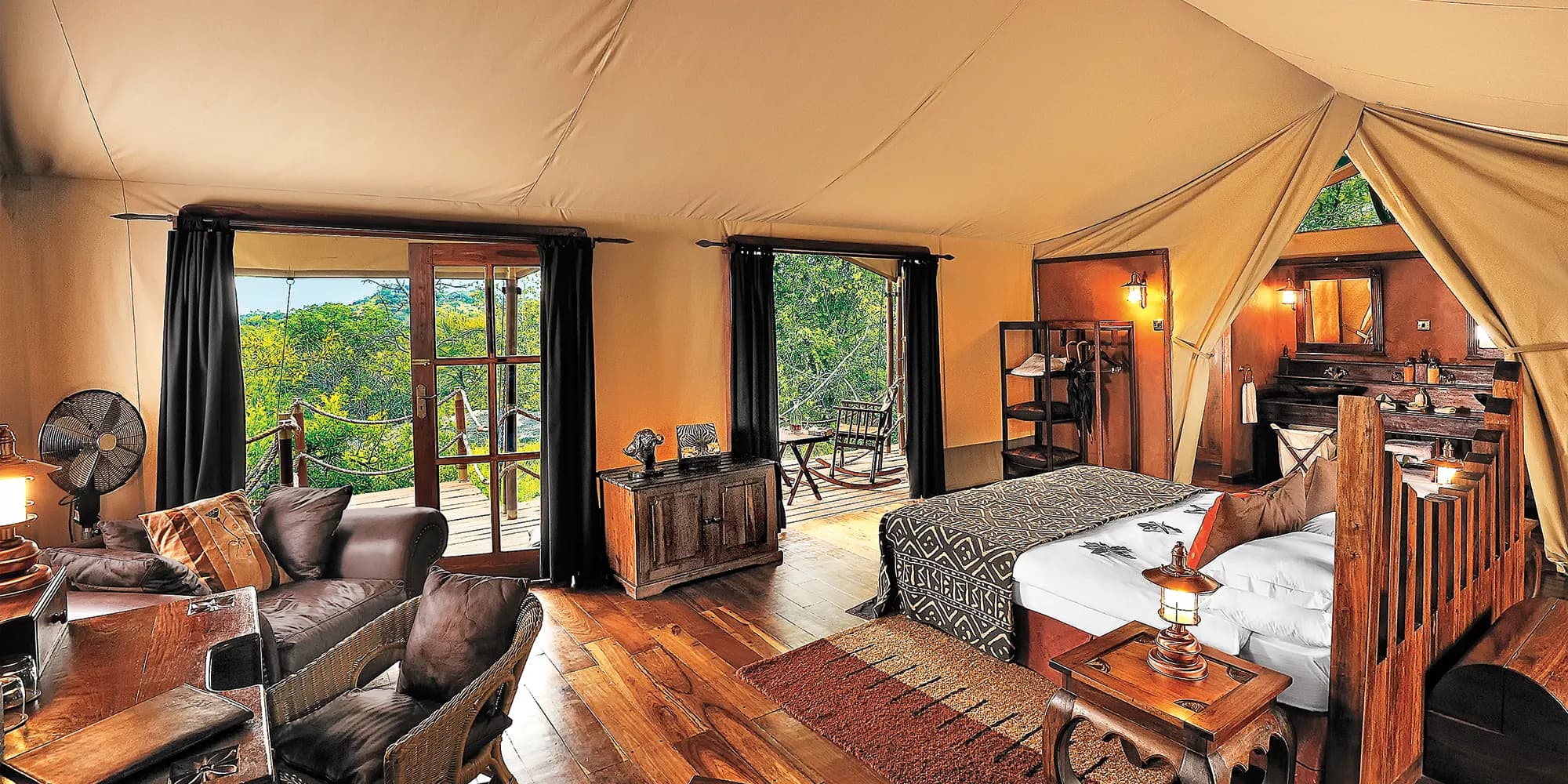 Interior of a luxury tented suite at Serengeti Migration Camp in Tanzania, with hardwood floors, a canopy bed and doors opening onto a private deck above the treetops